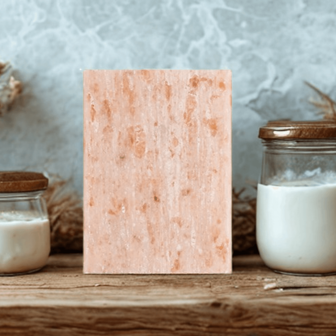Rectangular shaped miara essence goat milk natural soap on a wooden surface with jars of cream and goat's milk in the background.