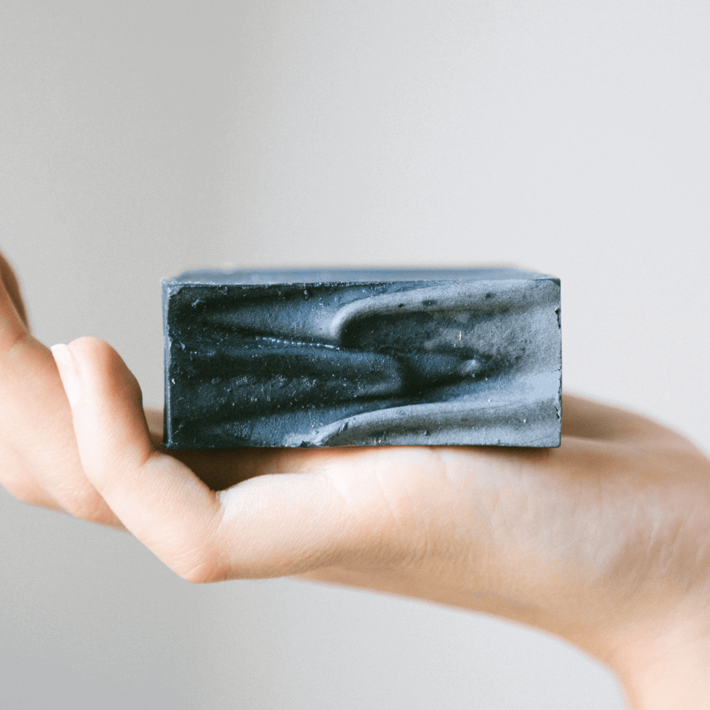 Miara Essence Activated Charcoal Soap displayed in hand, perfect for detoxifying skin and cleansing pores.